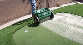 worker adding infill to artificial putting green